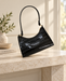 Black glossy crocodile-embossed shoulder bag with gold-tone strap links on a stone console.