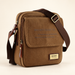 Brown canvas shoulder bag with printed flap and rectangular label on an ivory surface.