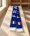 Blue France football scarf with tricolor patches and white fringes laid on a pale stone bench.