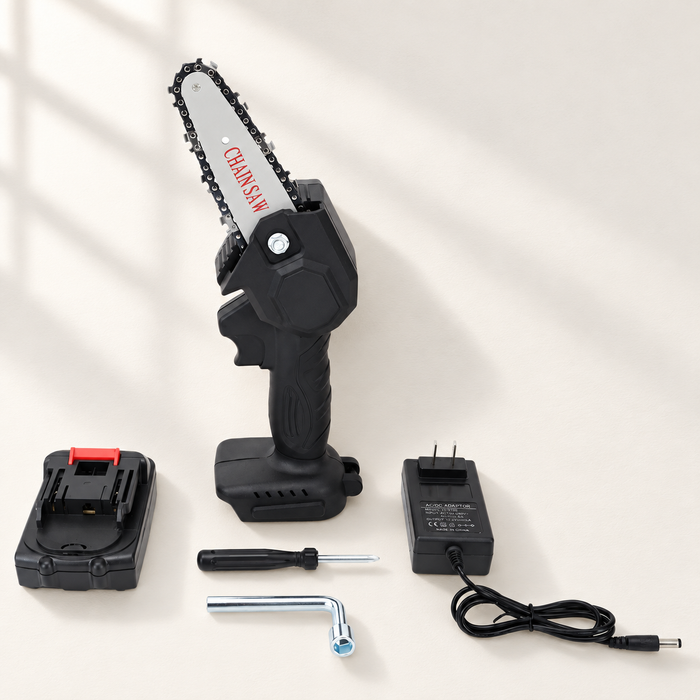 Mini chainsaw with battery, charger, screwdriver and socket wrench on an ivory surface