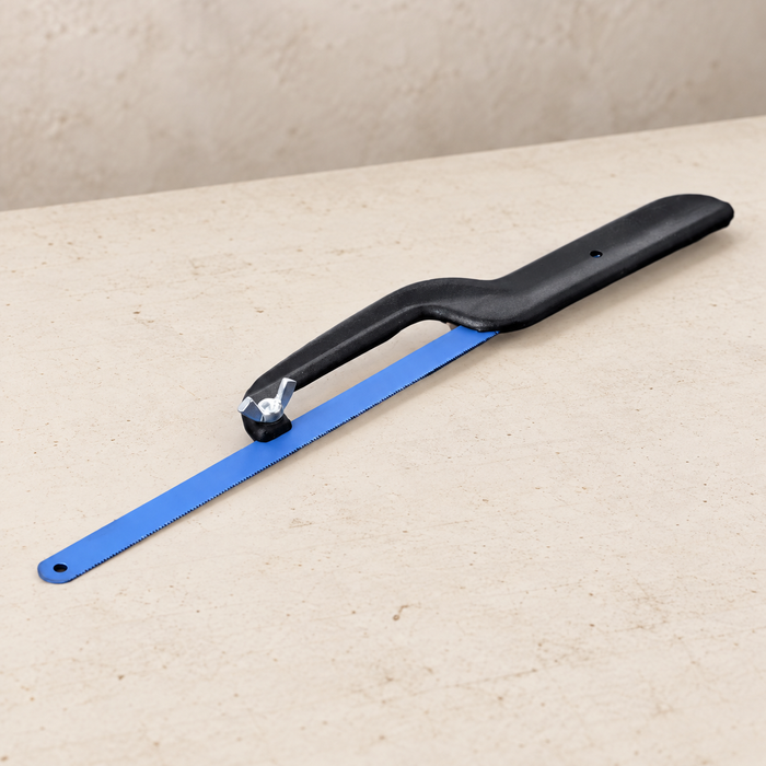 Compact black hacksaw with blue blade resting flat on an ivory workbench.