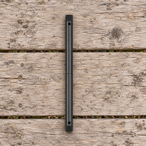 Black camping folding saw in its closed cylindrical form on a weathered wooden picnic table.