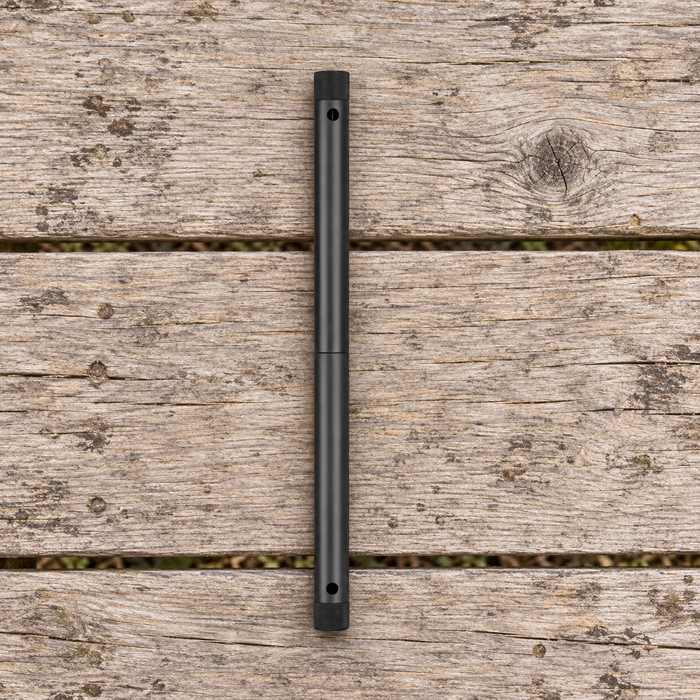 Black camping folding saw in its closed cylindrical form on a weathered wooden picnic table.