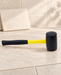 Black rubber mallet with yellow handle on a pale stone work surface.