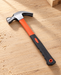 Orange and black claw hammer on a pale wooden workbench.
