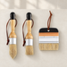 Three wooden handled paint brushes arranged on a warm ivory surface.