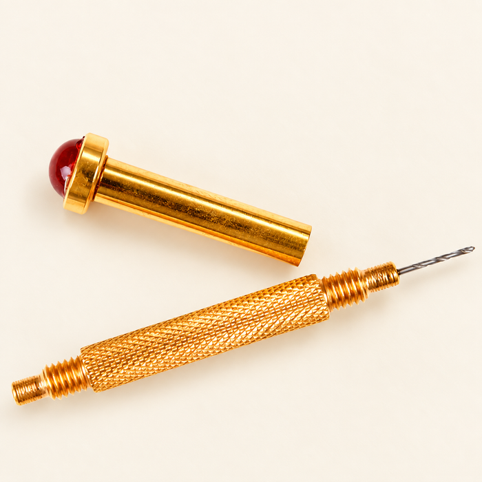 Gold manual nail drill with red cap on ivory surface