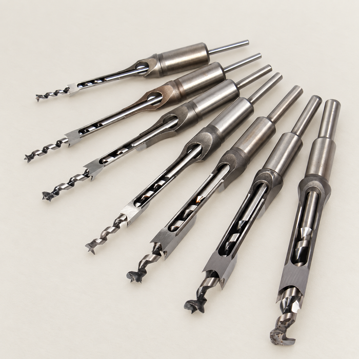 Seven square-hole woodworking drill assemblies on an ivory work surface.