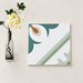 Green and white patterned square tile beside a floral vase