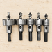 Five metal hole-saw drill bits resting on a light workbench