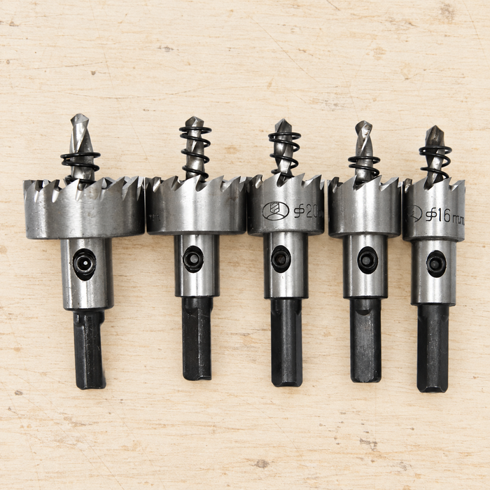 Five metal hole-saw drill bits resting on a light workbench