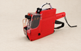 Red manual price labelling machine on an ivory surface.