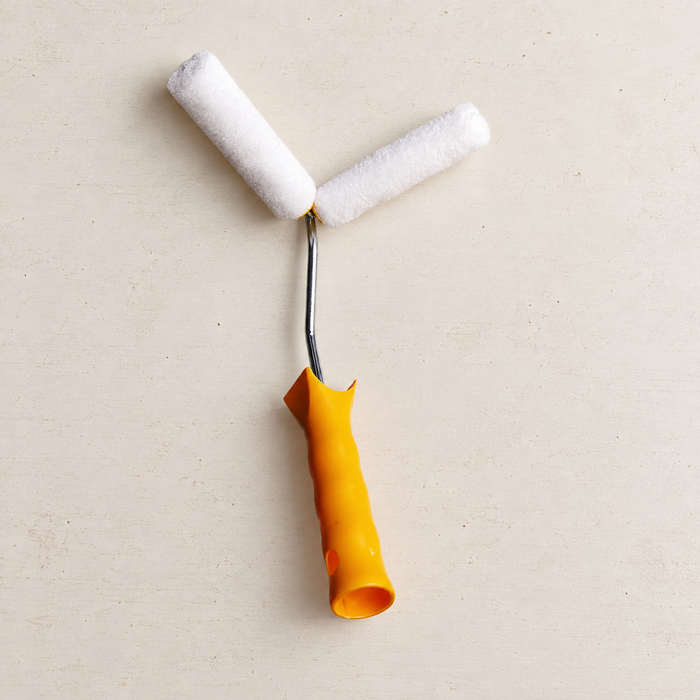 Yellow-handled corner paint roller with two white rollers on an ivory workbench.