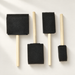Four foam paint brushes with wooden handles arranged on an ivory surface