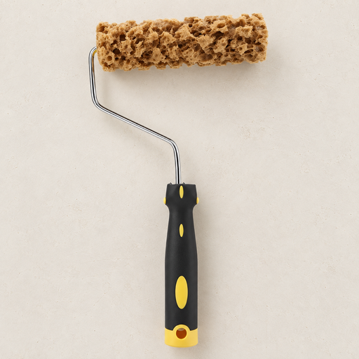 Tan sponge texture paint roller with a black and yellow handle on an ivory workbench.