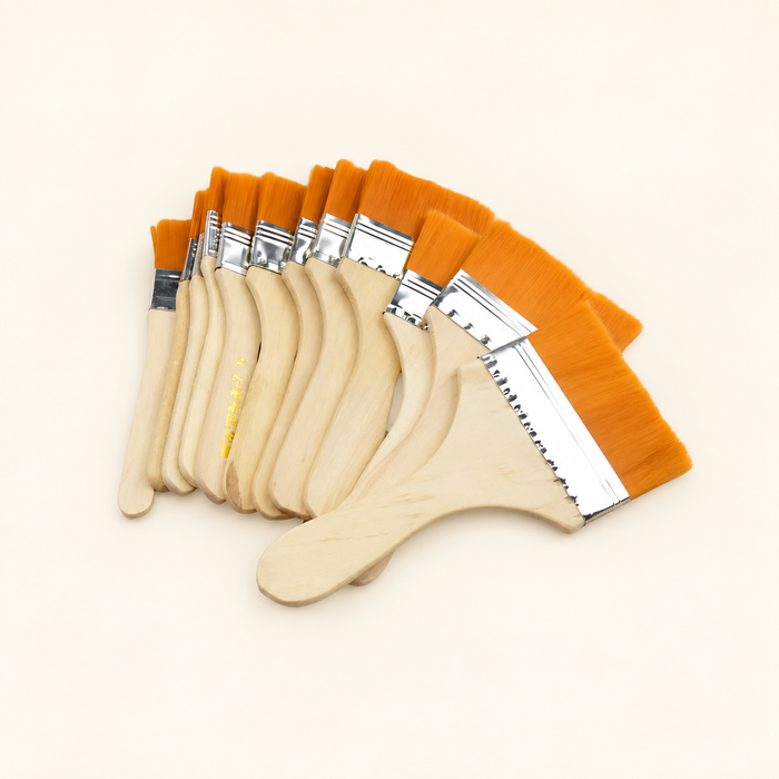 Orange-bristle paint brushes with wooden handles arranged in a fan on an ivory surface
