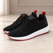 Black sneakers with white midsoles and red trim resting on an ivory floor.