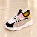 Multicolour sneaker with pink tongue and yellow collar on pale stone.