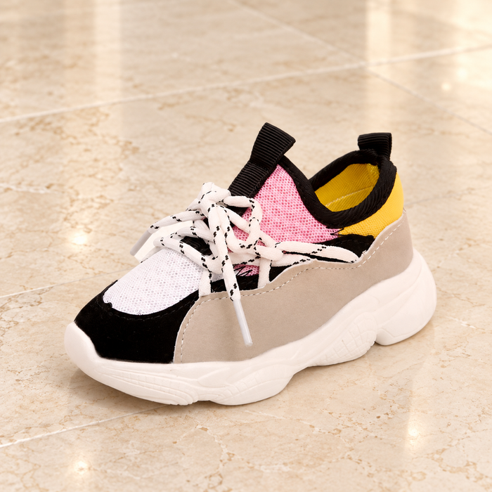 Multicolour sneaker with pink tongue and yellow collar on pale stone.