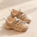 Pair of beige knit shoes with cord toggles on pale stone.