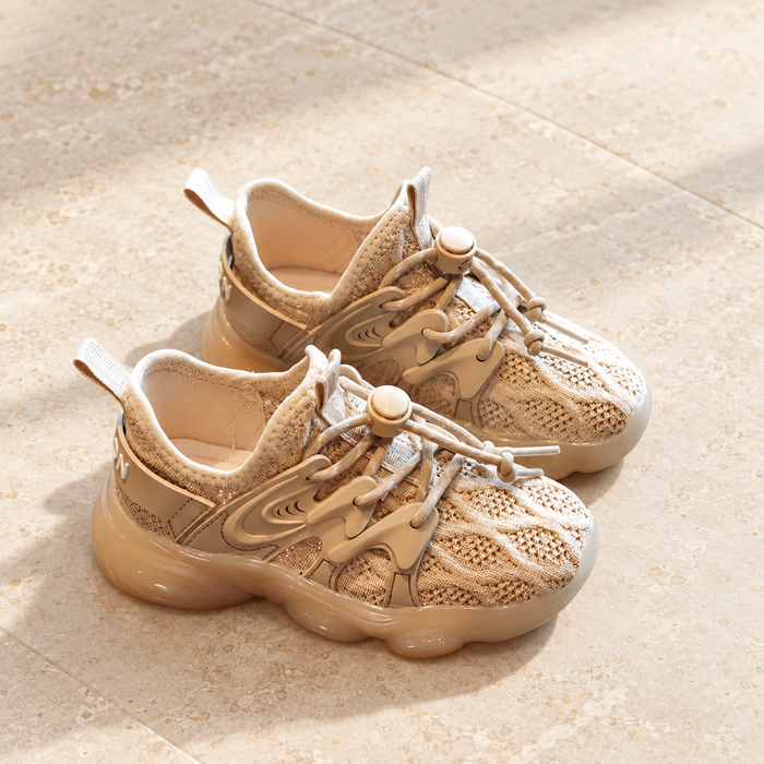 Pair of beige knit shoes with cord toggles on pale stone.
