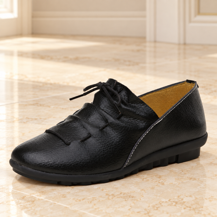 Black lace-up shoe with tan lining on pale ivory stone.