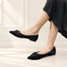 Black pointed flats with twisted toe details worn with a black skirt