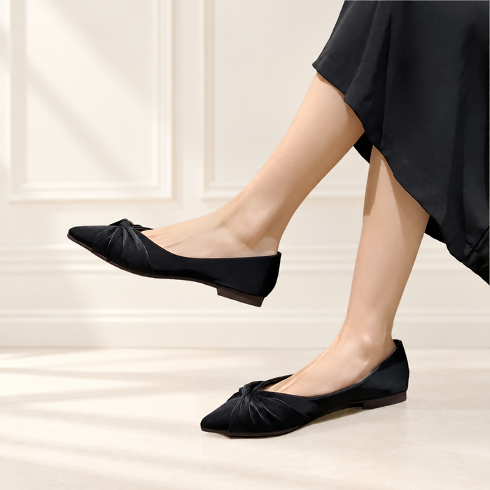 Black pointed flats with twisted toe details worn with a black skirt