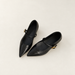 Black pointed shoes with thin straps and gold buckles on an ivory floor