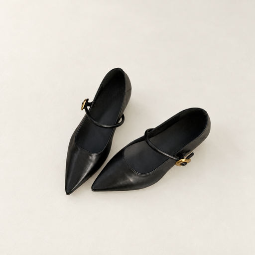 Black pointed shoes with thin straps and gold buckles on an ivory floor
