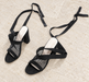 Pair of black mesh block-heel sandals with long ties on ivory stone.