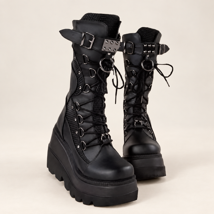 Black platform boots with studded straps and lace hardware on an ivory floor