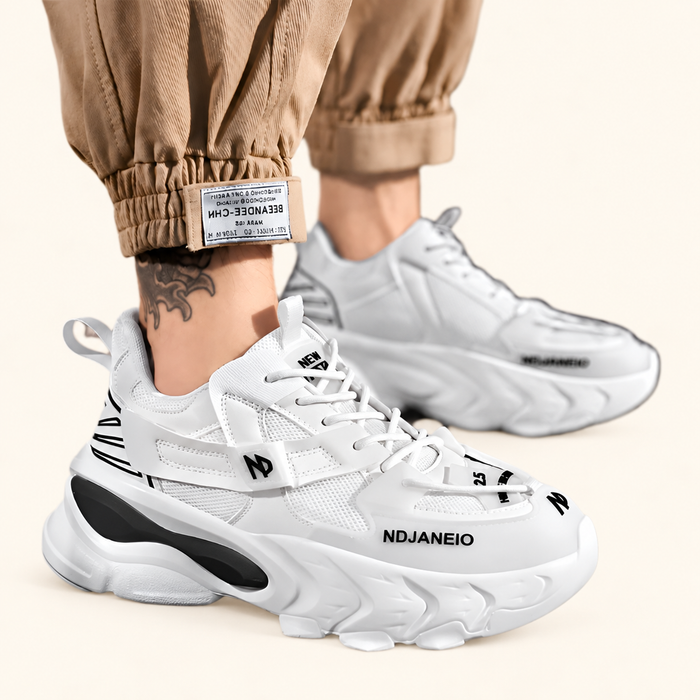 White mesh sneakers with black lettering and chunky soles worn with beige trousers