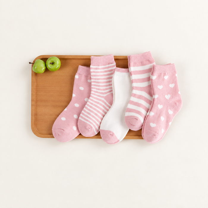 Five pink and white baby socks on a wooden tray with green apples