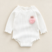 White ribbed baby bodysuit with pink bunny patch on ivory surface