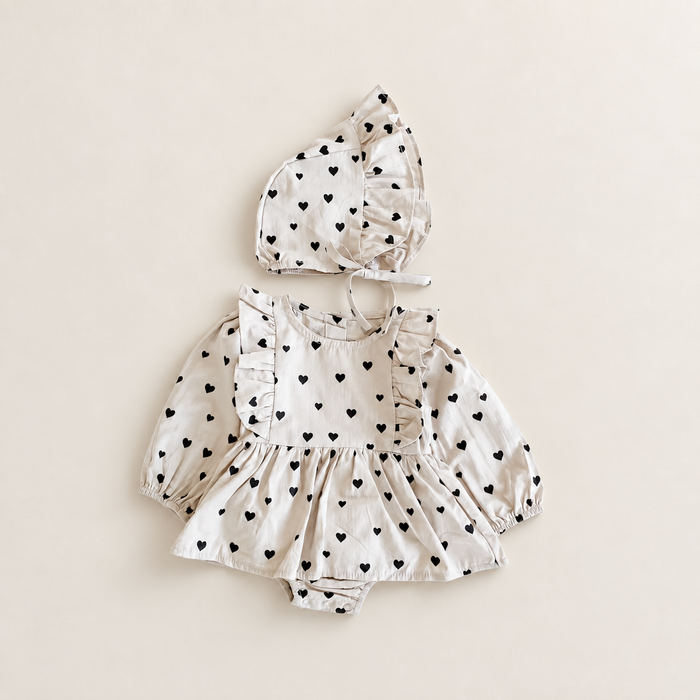 Ivory heart print baby romper and matching bonnet on ivory tabletop