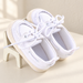 White canvas baby shoes with cream woven soles on a small ivory stool