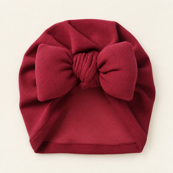 Burgundy baby bow beanie on ivory tabletop