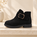 Black suede ankle boot with gold buckle on an ivory stone shelf.