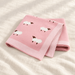 Folded pink knitted sheep blanket on ivory linen.