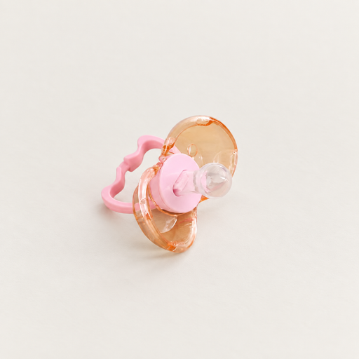 Pink pacifier with an amber translucent shield on an ivory surface.
