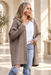 Taupe hooded knit cardigan worn over a white top and jeans in an ivory interior